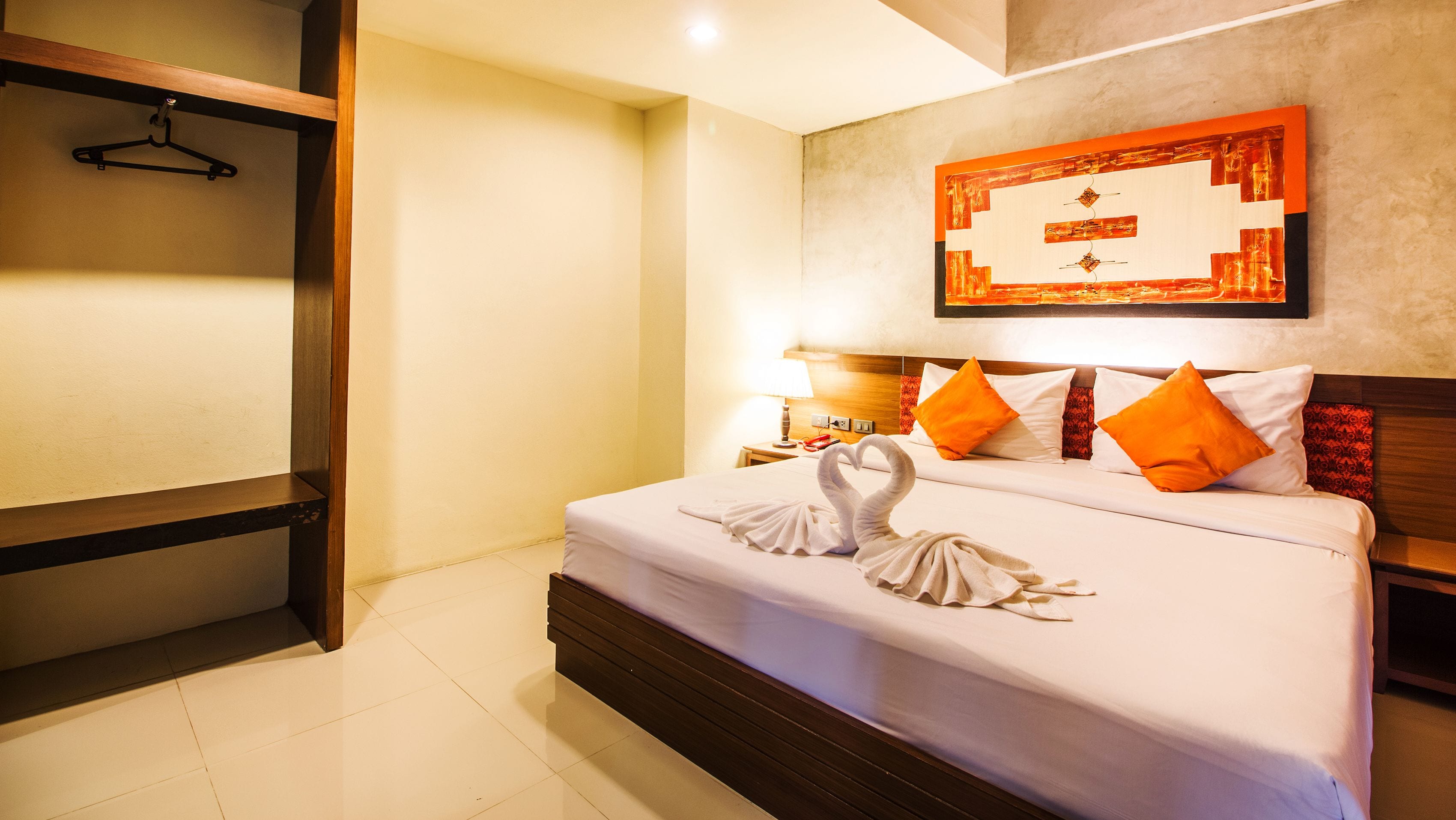 A hotel room with a bed, a wooden headboard, a wall-mounted artwork, and a hanging coat rack.
