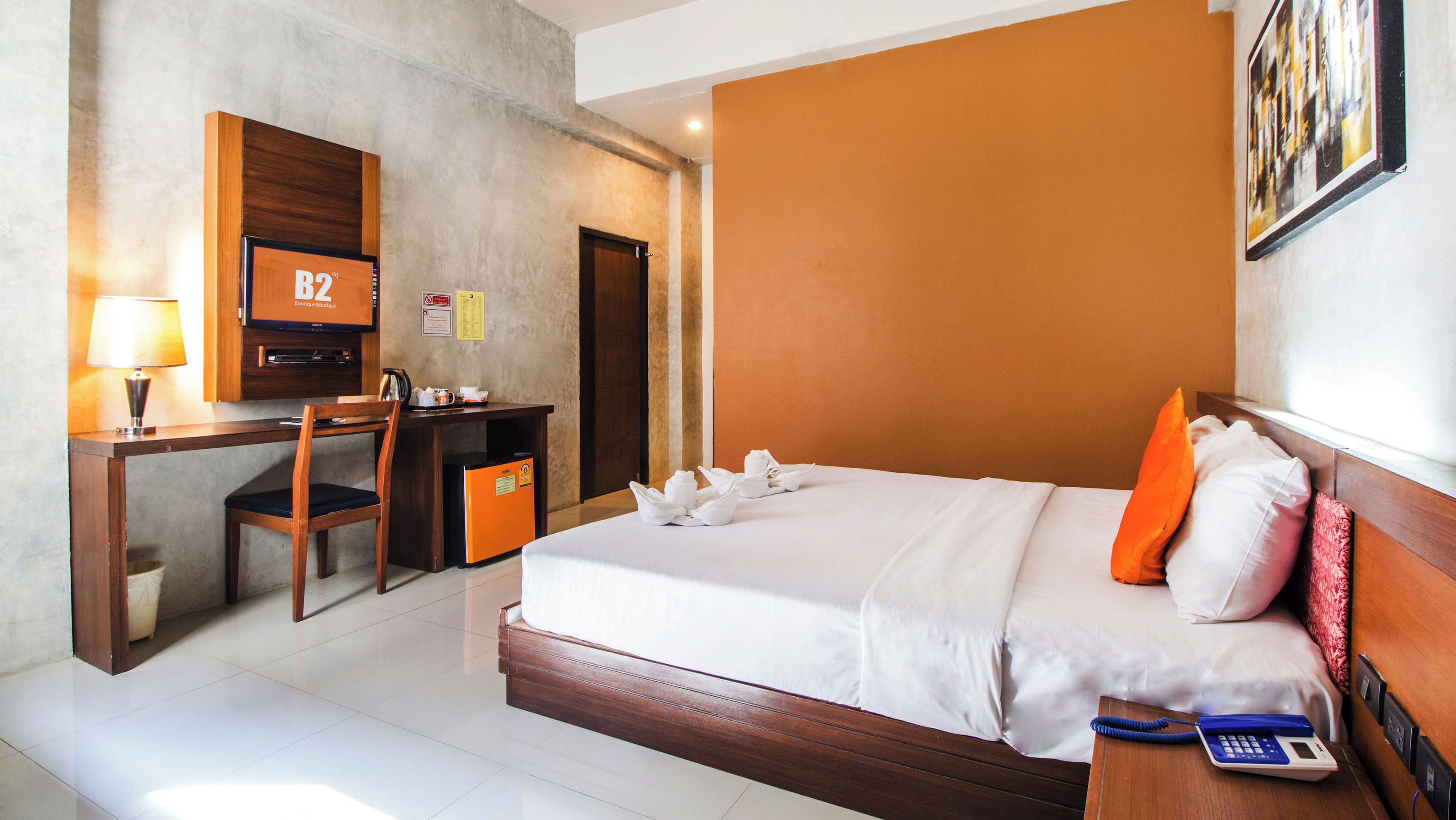 A hotel room with a bed, a desk with a computer, a telephone, and a TV.