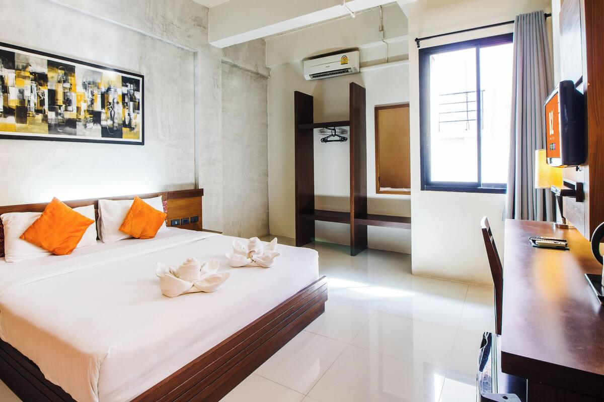 A hotel room with a large bed, a desk, a TV, and a painting on the wall.