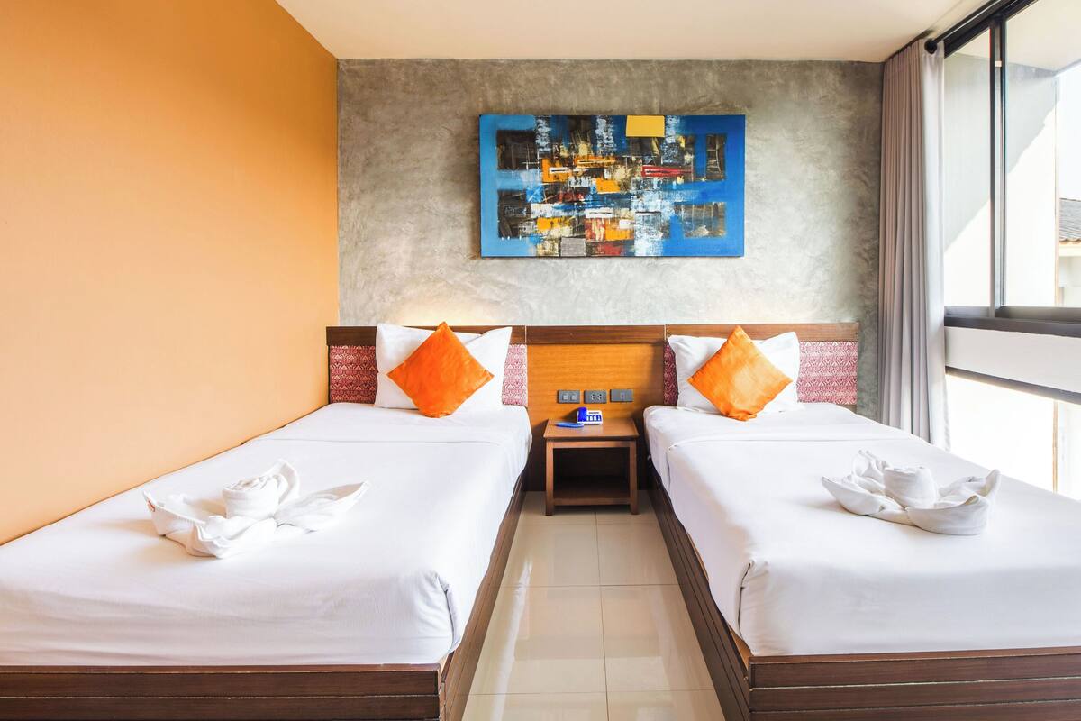 A hotel room with two beds, a painting on the wall, and a window with a view.