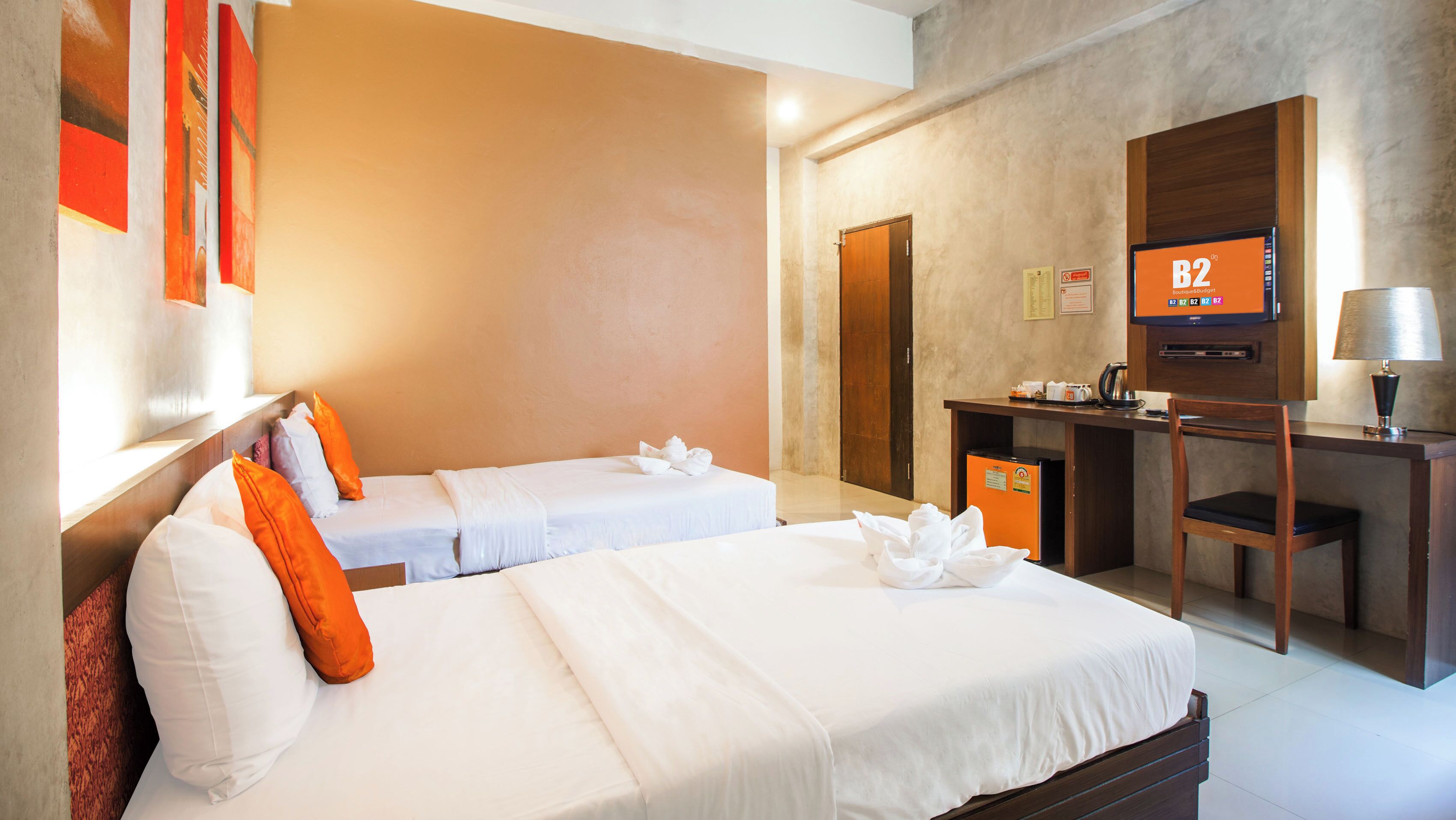 A hotel room with two beds, a desk with a computer, a TV, and a lamp.