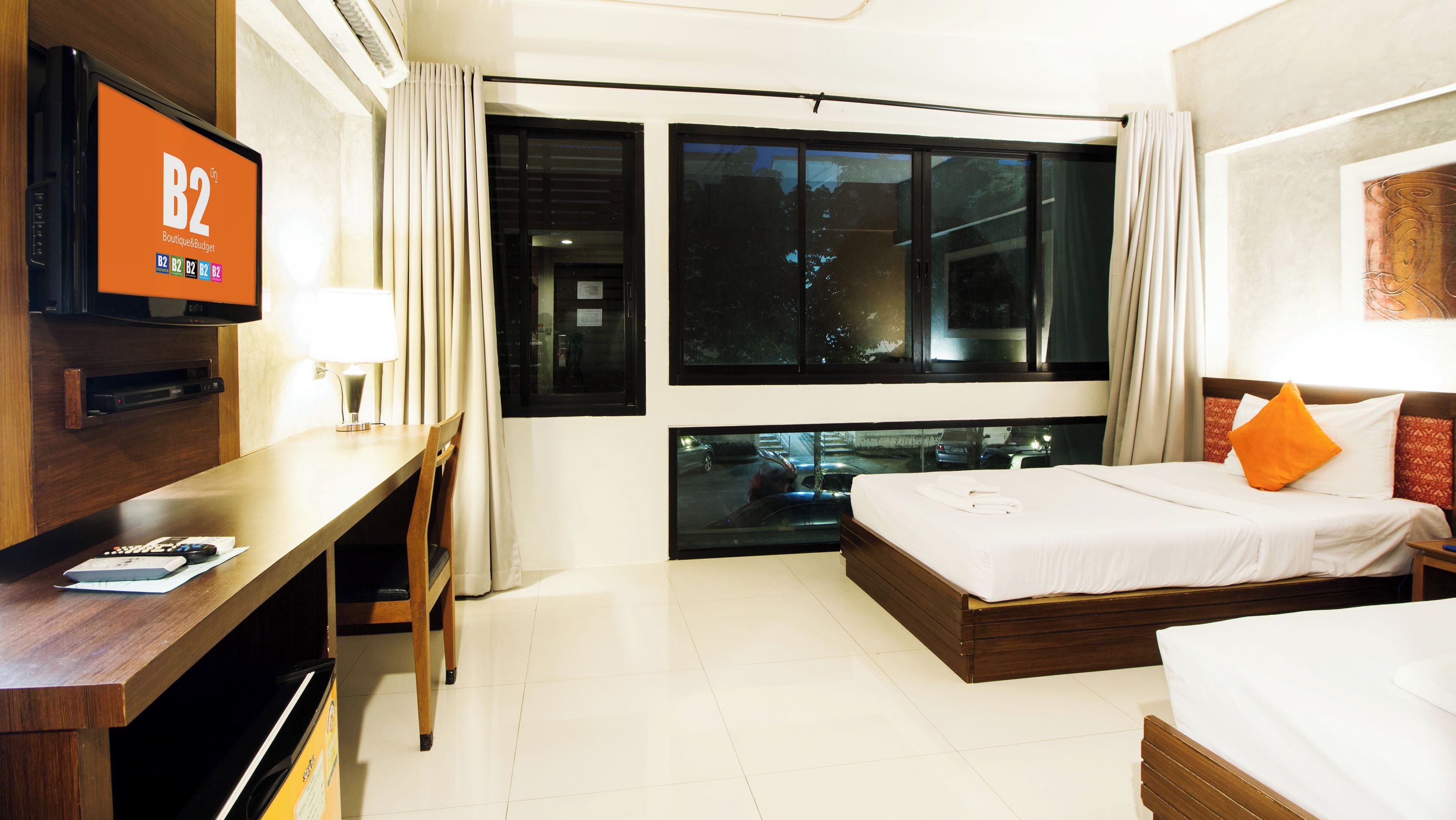 A hotel room with a bed, a desk, a TV, and a large window.