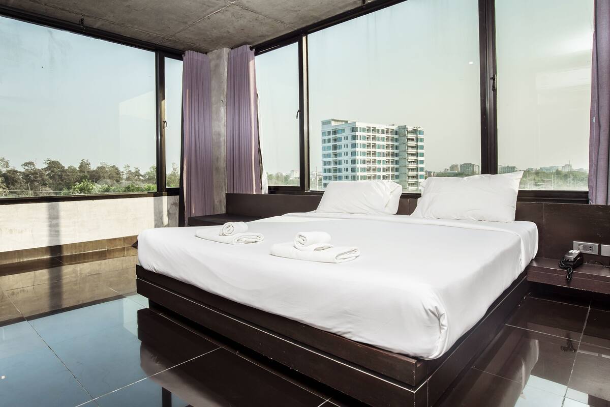 Une chambre d’hôtel moderne avec un grand lit, une vue sur le paysage urbain et un balcon doté d’une balustrade.