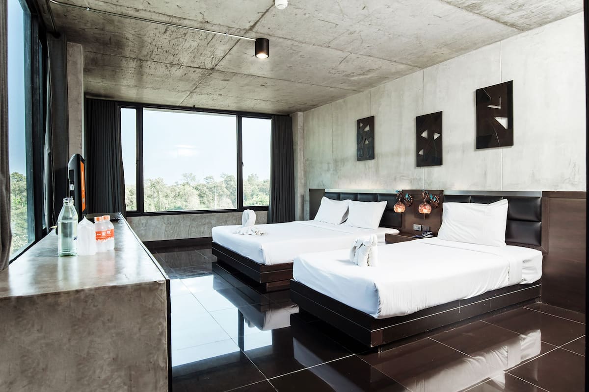 Une chambre d’hôtel moderne avec deux lits, une grande fenêtre et un plafond en béton.