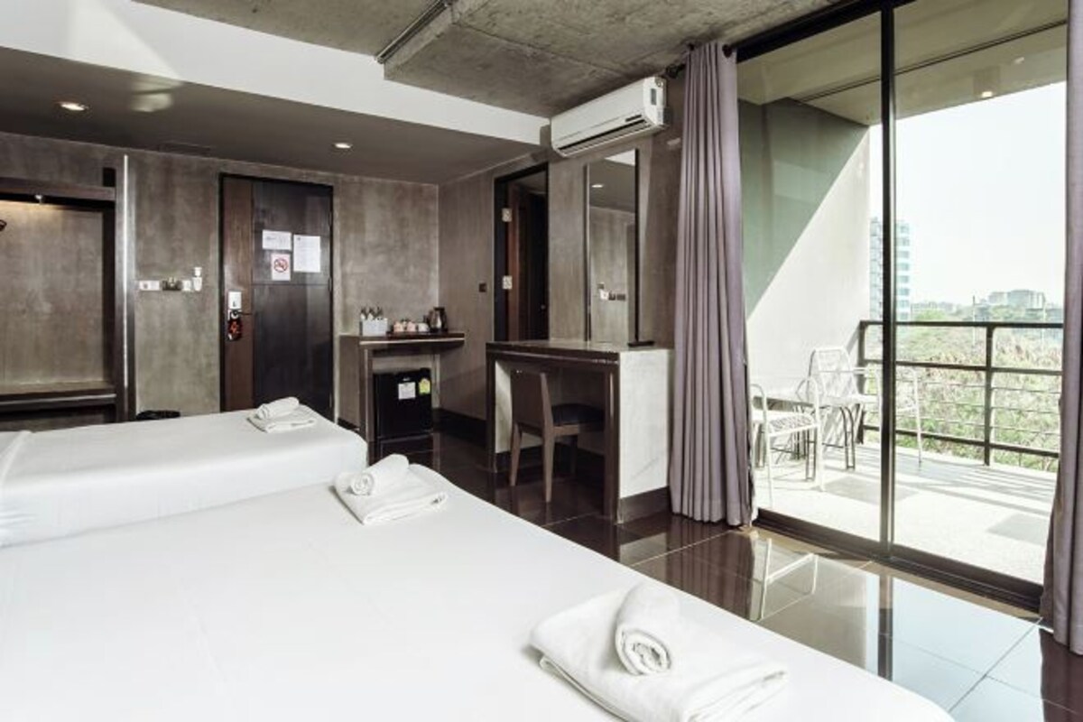 Une chambre d’hôtel moderne avec deux lits, un bureau et un balcon offrant une vue agréable.