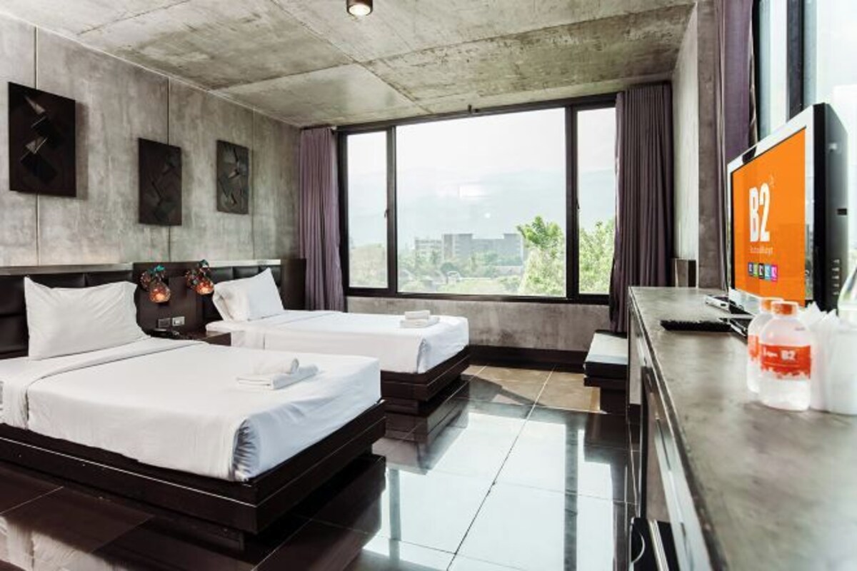 Une chambre d’hôtel avec deux lits, une grande fenêtre donnant sur la ville, un téléviseur à écran plat et un minibar.