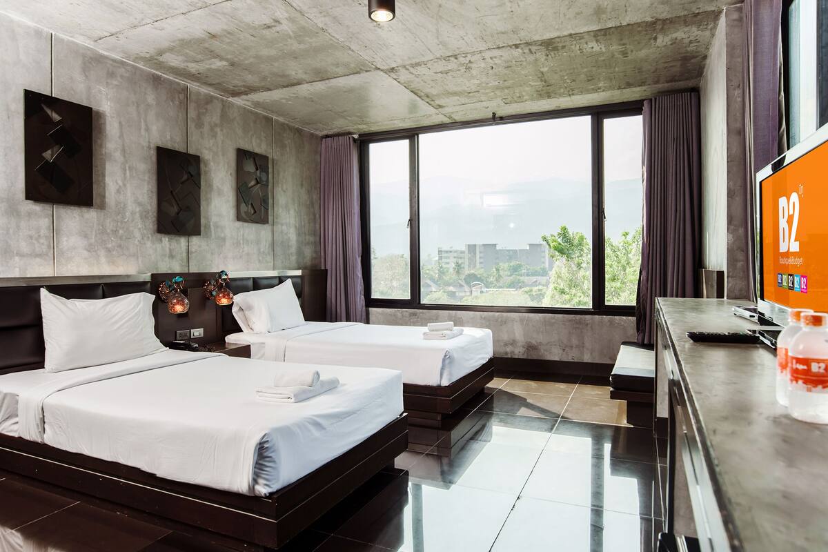 Une chambre d’hôtel avec deux lits, une grande fenêtre donnant sur la ville, un téléviseur à écran plat et un minibar.