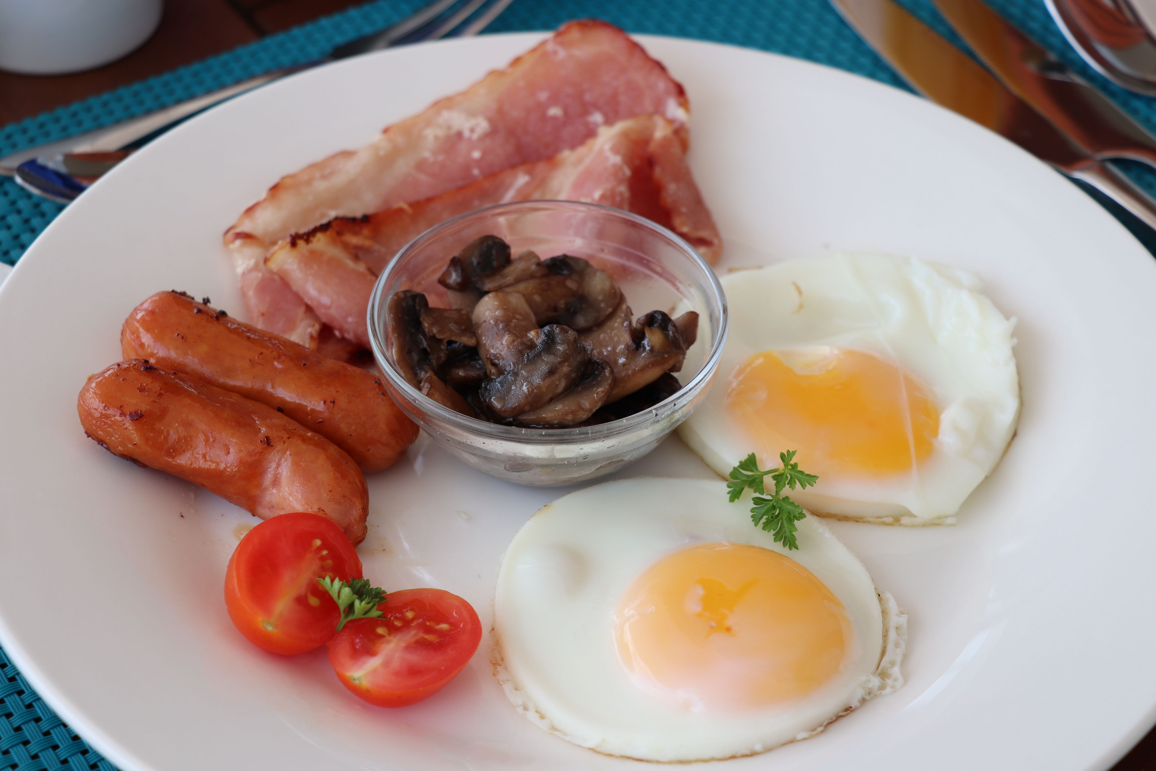A plate with bacon, sausages, mushrooms, eggs, and tomatoes.