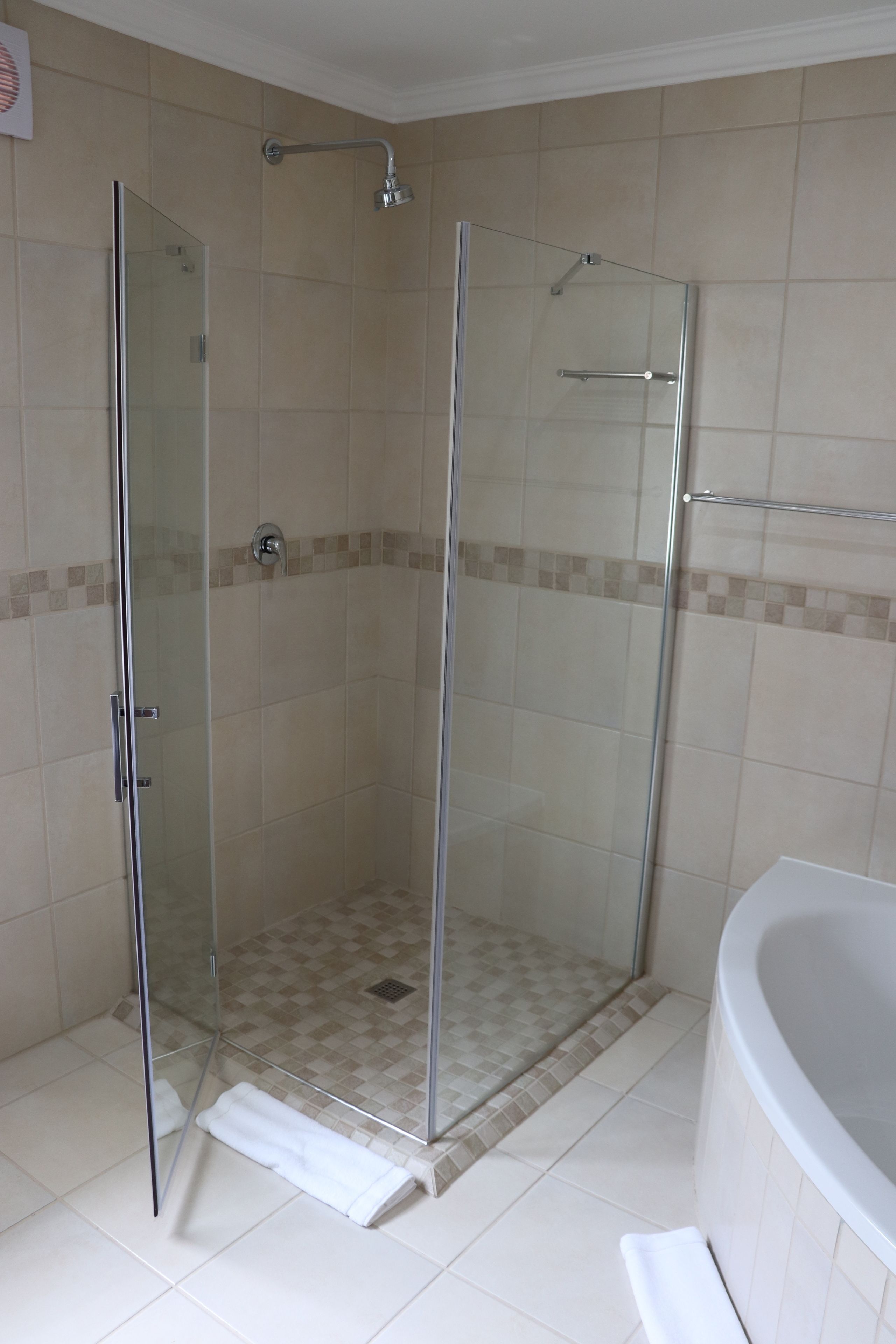 A glass-enclosed shower with a white bathtub and beige tiles.