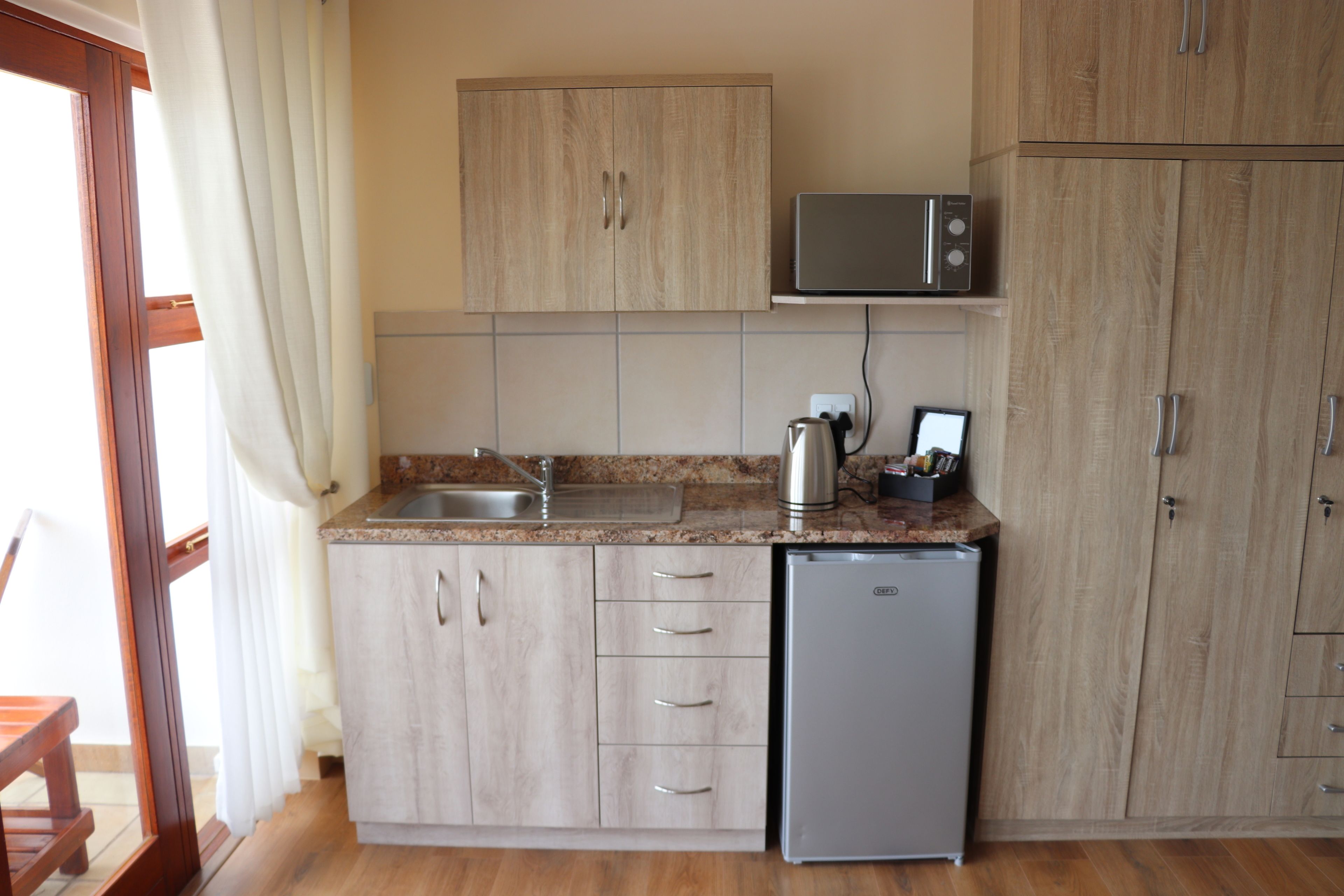 A compact kitchen with wooden cabinets, a built-in microwave, a small refrigerator, and a sink.
