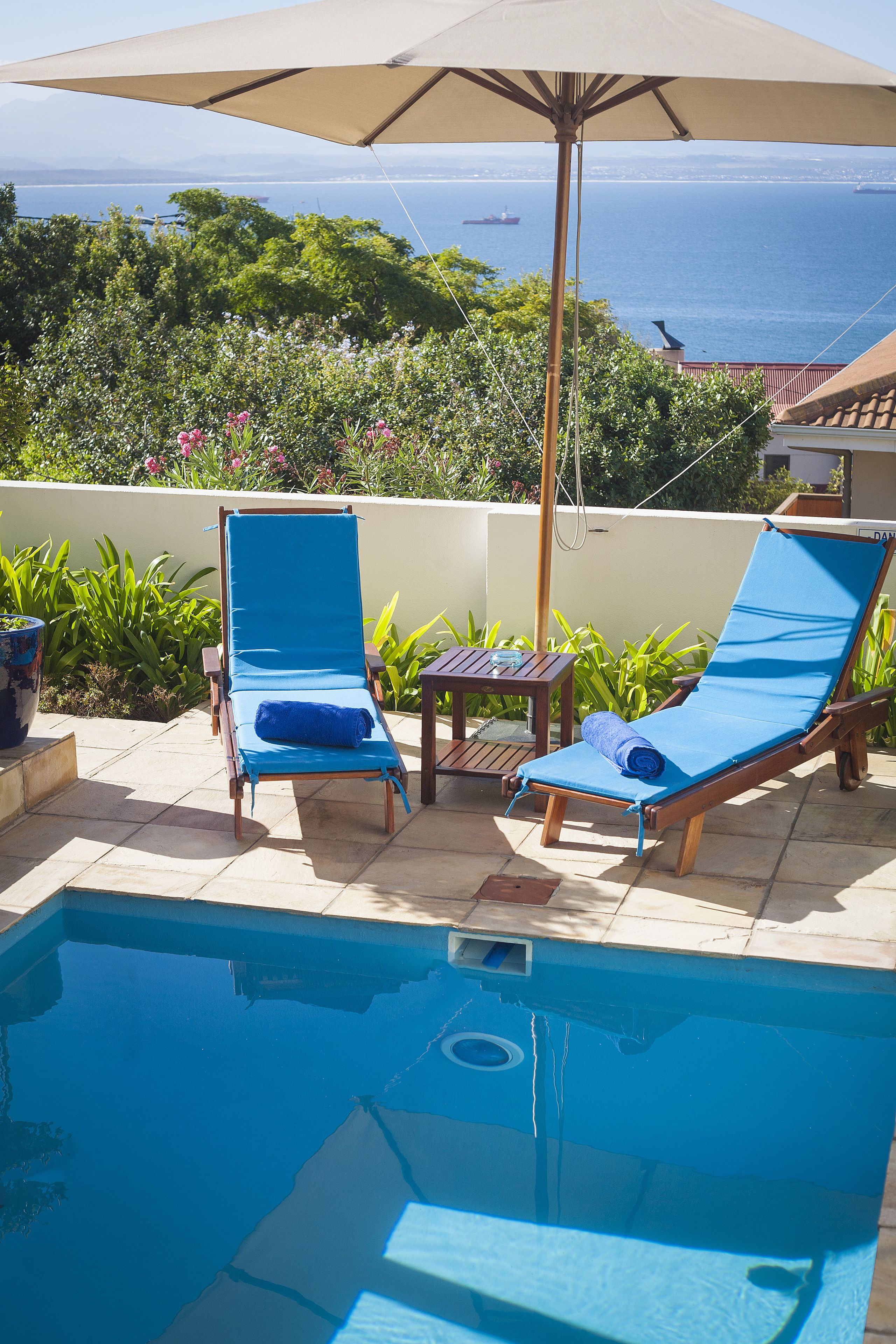 Un espace aménagé au bord de la piscine, avec deux chaises longues bleues, une table et un parasol.