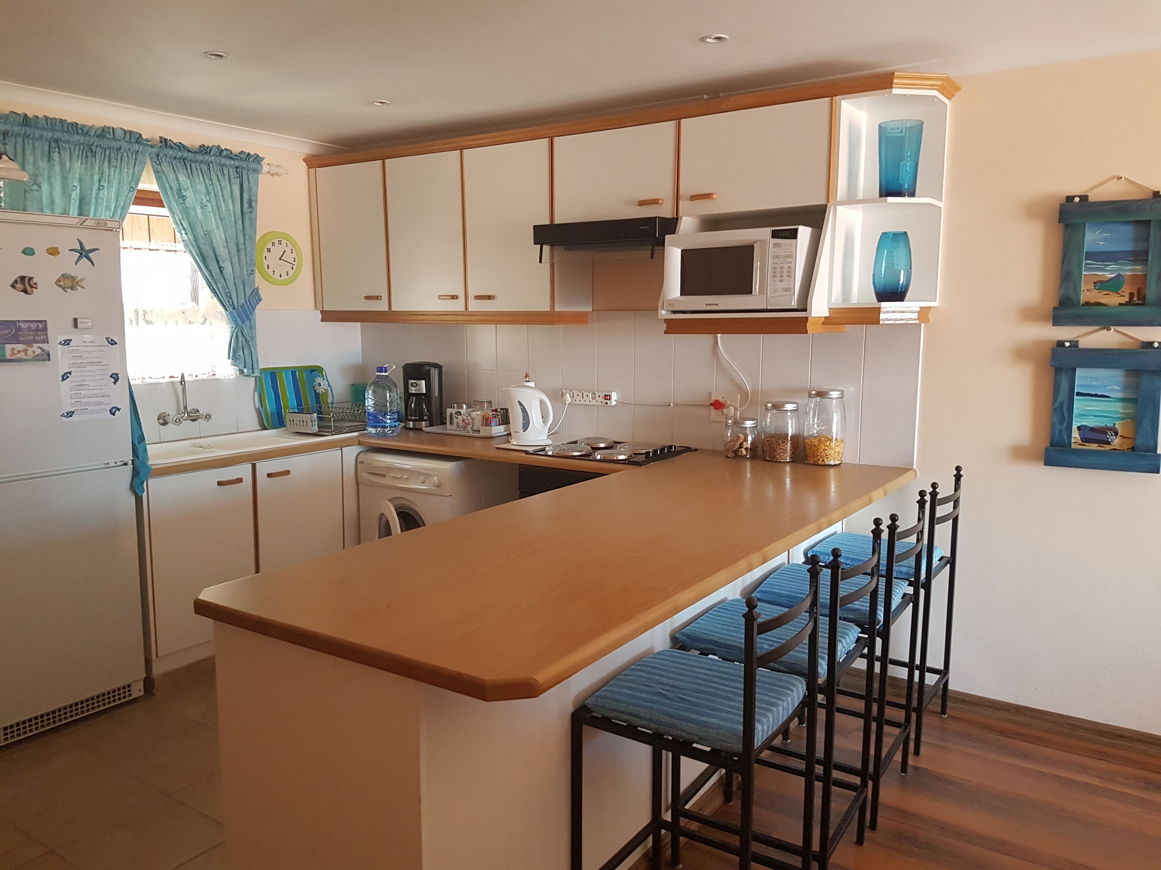 Una cocina con encimera de madera, taburetes de bar, microondas, fregadero y lavadora.