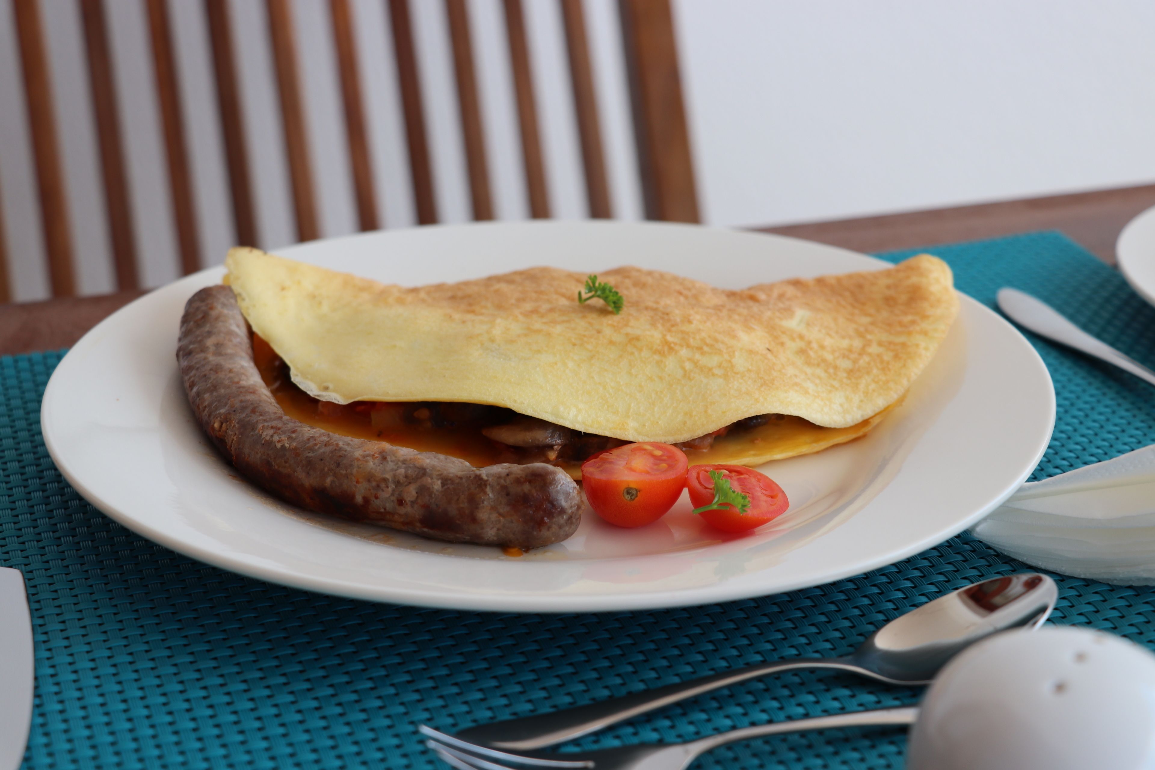 A plate with a folded omelette, sausage, and tomatoes on a white plate.