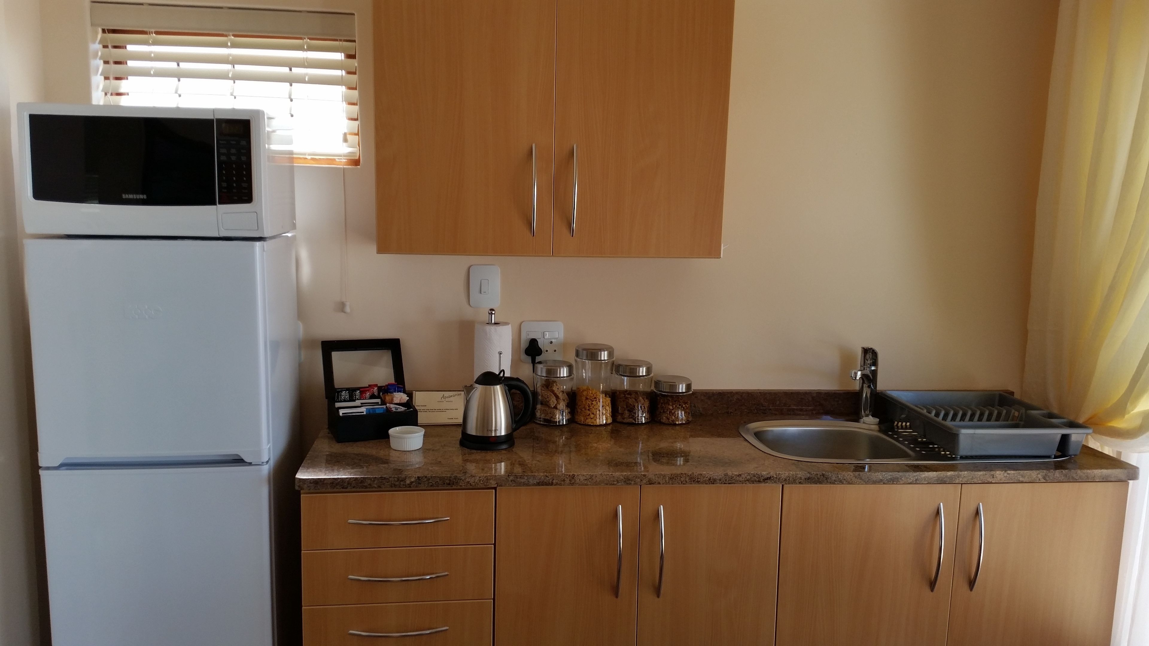 A compact kitchen with a microwave, coffee maker, and various jars on the counter.