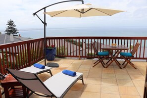A balcony with a table and chairs, a large umbrella, and a view of the ocean.