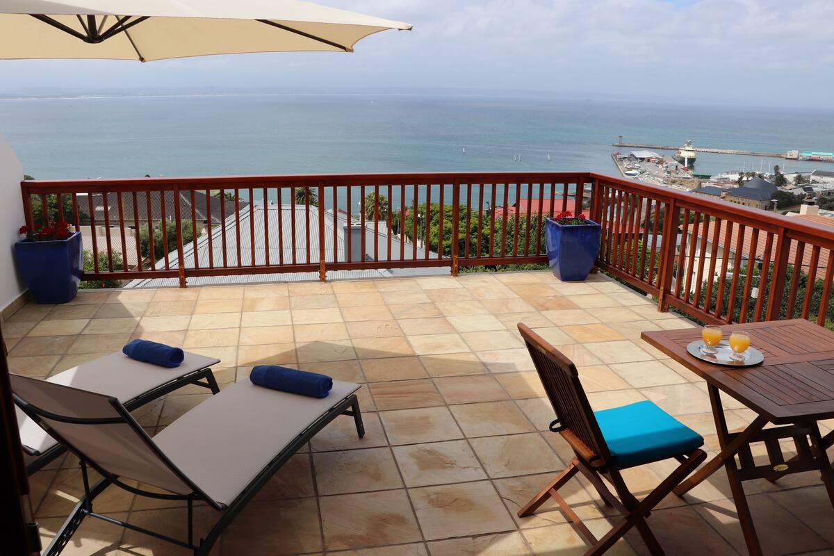 Un balcon avec vue sur la mer, une table avec deux chaises et une poubelle bleue.