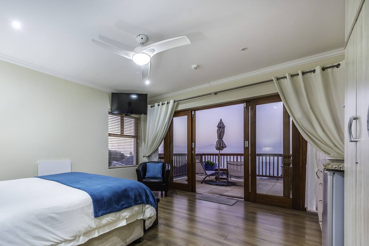 Une chambre avec un lit, un ventilateur de plafond, une télévision et un balcon avec vue.