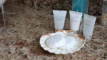 Un plan de travail en granit sur lequel reposent trois tubes de produits de toilette étiquetés « gel douche », « lotion pour le corps » et « shampoing », ainsi qu’un récipient en forme de coquillage.