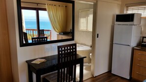 Une cuisine compacte équipée d’un réfrigérateur, d’une table à manger avec des chaises, d’un miroir et offrant une vue sur la mer par une fenêtre.