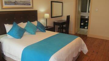 Une chambre d’hôtel avec un lit, un bureau, une chaise, une lampe et une salle de bain visible à travers une porte ouverte.