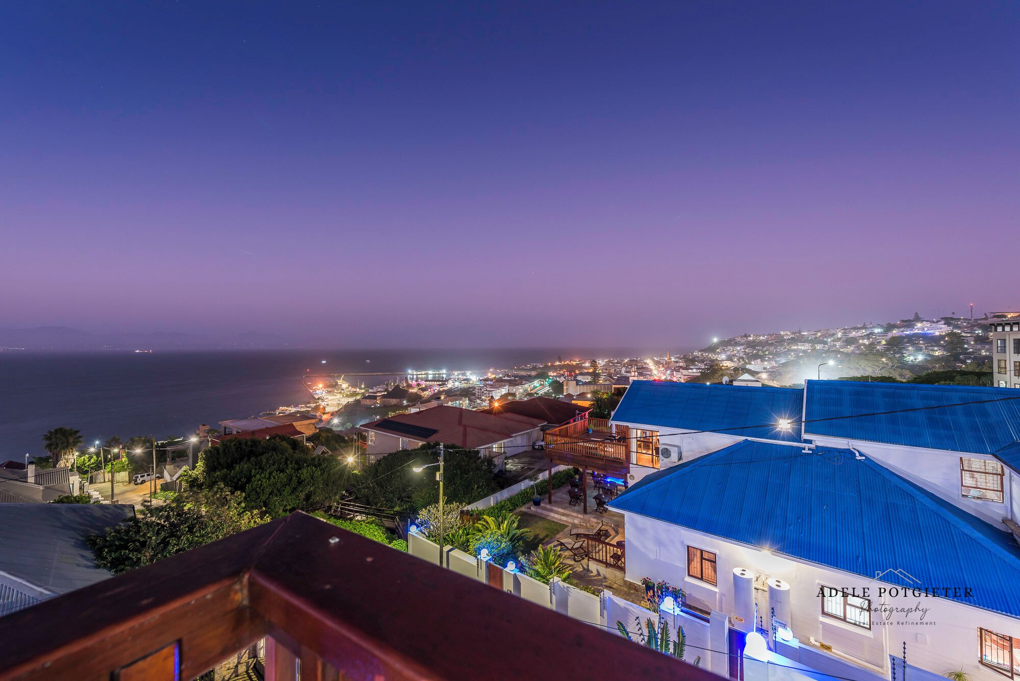 A coastal town at dusk with illuminated buildings and a view of the sea.