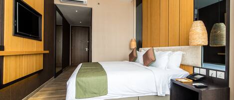 A modern hotel room with a bed, bedside table, TV, and a large mirror.