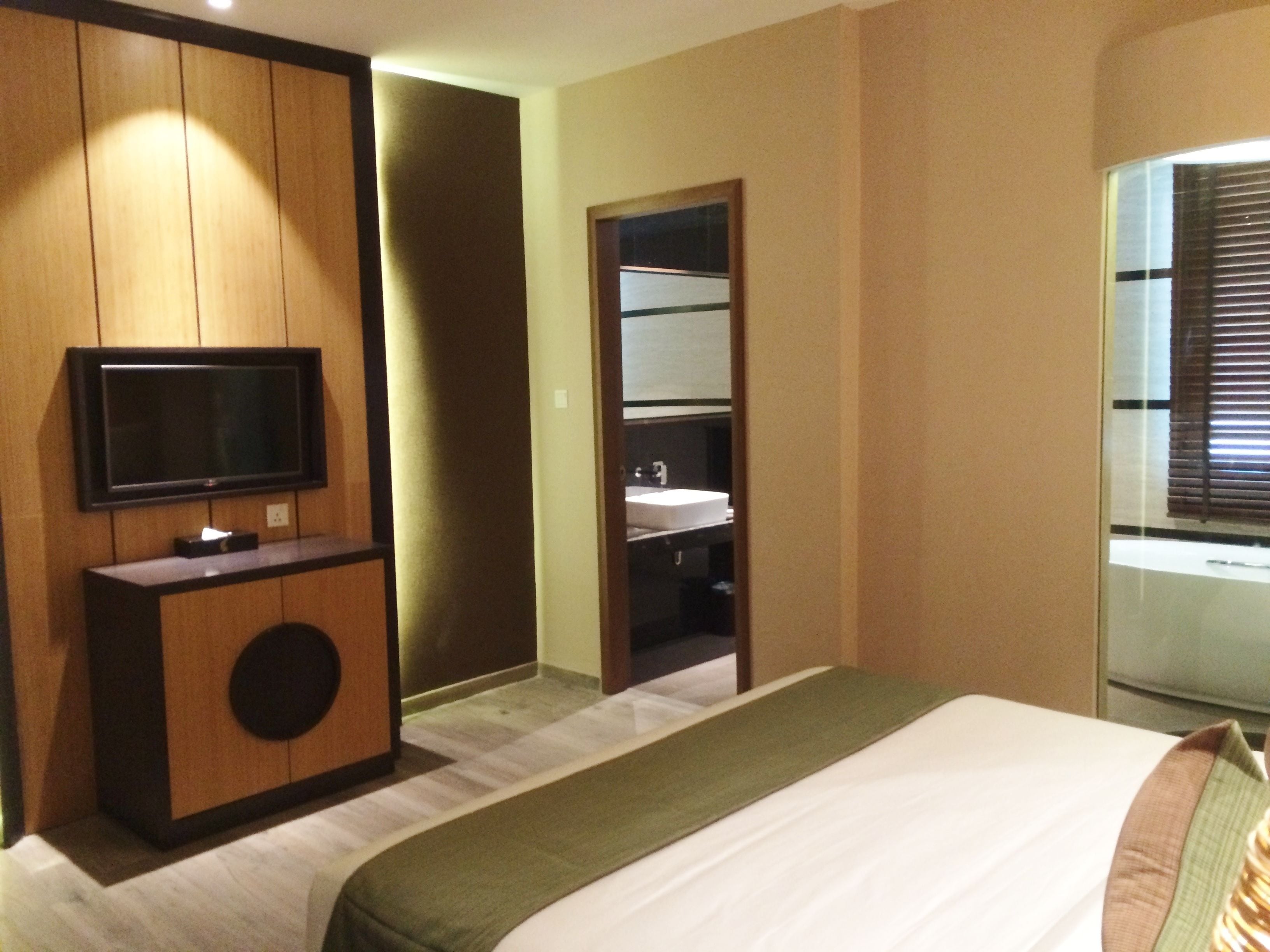 Une chambre d’hôtel comprenant un lit, un téléviseur fixé à un meuble en bois, une salle de bain avec un lavabo et un miroir.