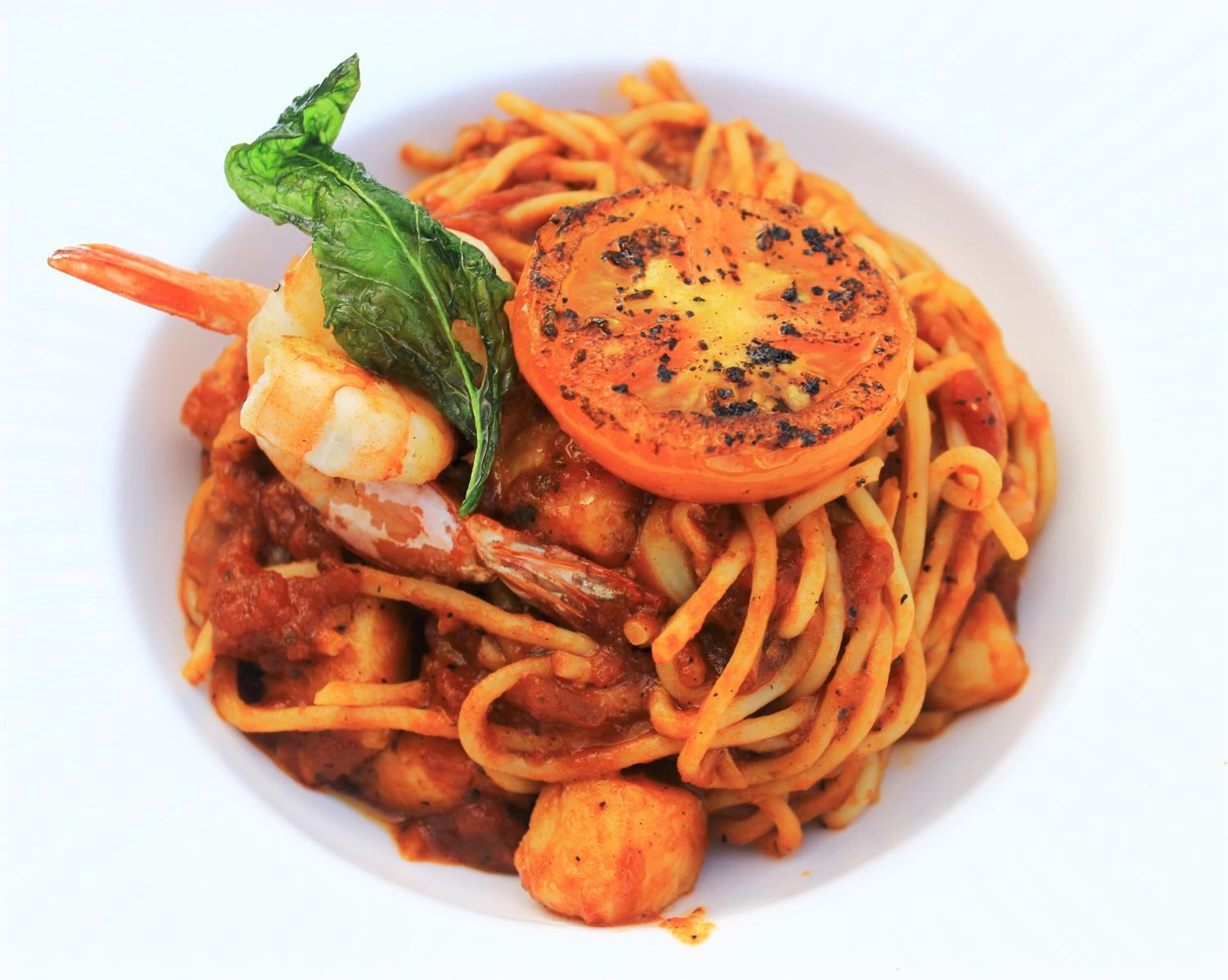 A plate of spaghetti with shrimp, tomato slices, and basil.