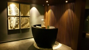 A reception desk with a dark, curved design, a wooden slat wall, and four wall-mounted leaf-shaped light fixtures. - Eska Hotel (Batam)
