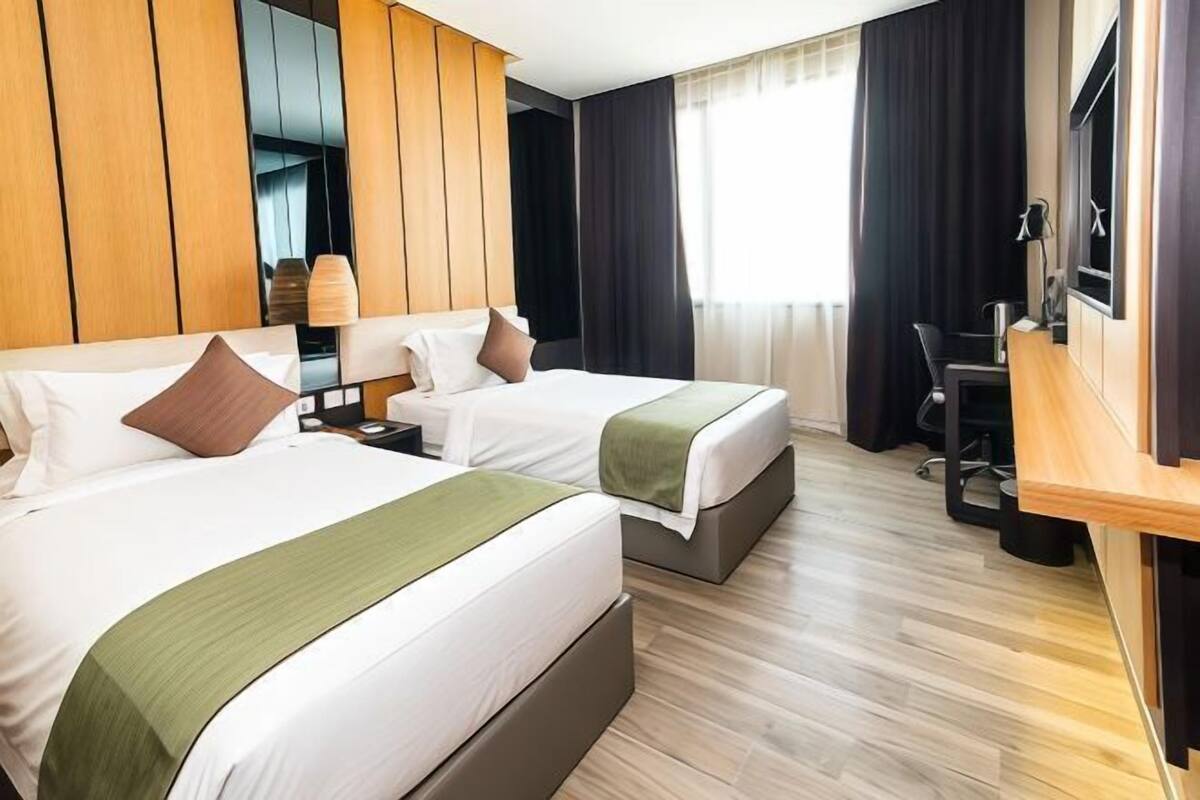 A hotel room with two beds, a desk, and a mirror.