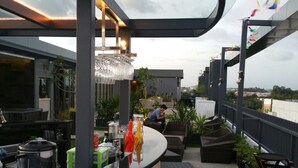 A rooftop bar with a glass enclosure, outdoor seating, and a view of the cityscape. - Eska Hotel (Batam)