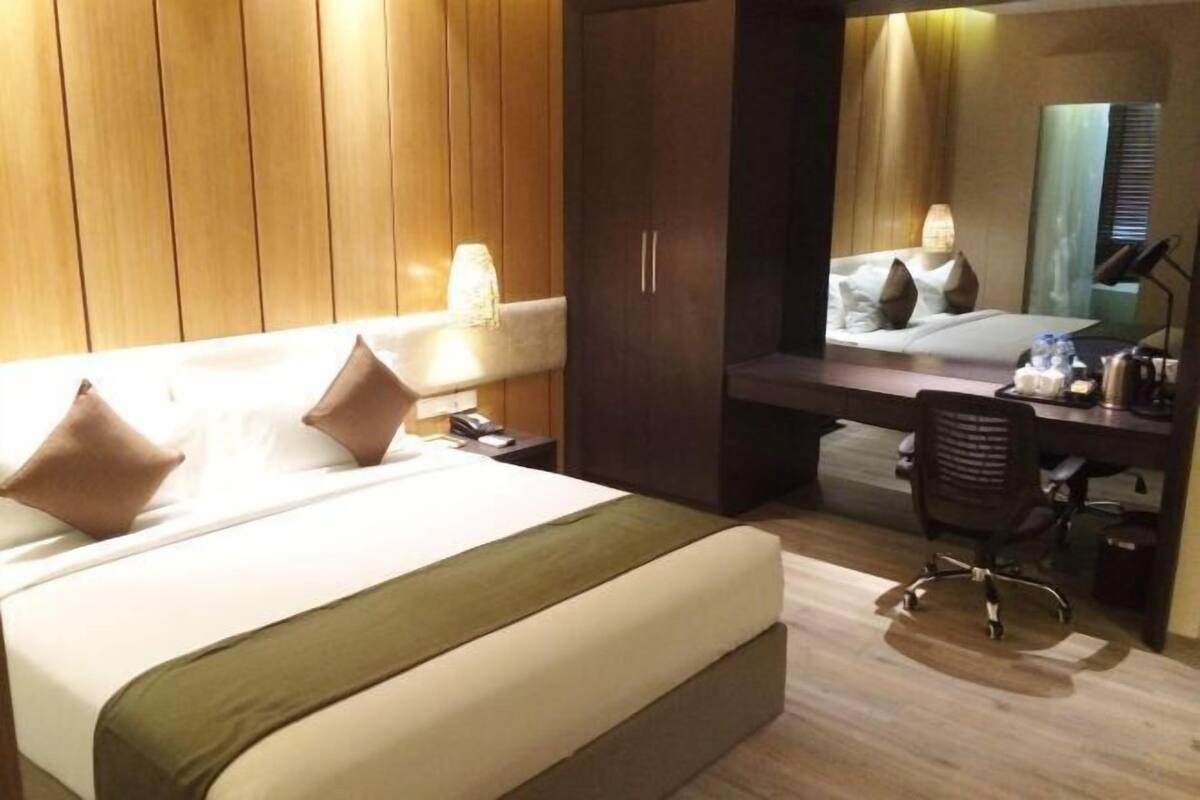 A hotel room with a bed, a desk, a chair, a wardrobe, and a mirror.
