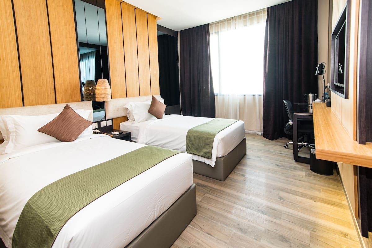 A hotel room with two beds, a desk, a chair, and a large window with curtains.