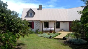 A single-story house with a sloped metal roof, a front porch, and a small garden area with flowers and shrubs.