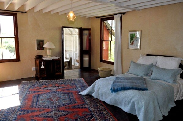 Un dormitorio con una cama grande, un tapete estampado, suelo de madera y vistas al exterior a través de una puerta.