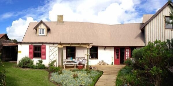 Une maison de plain-pied avec un toit en pente, un porche à l’avant et un petit jardin agrémenté d’un chemin menant à l’entrée.