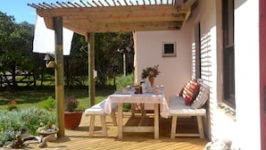 An outdoor patio with a wooden table and chairs, a pergola, and a potted plant.