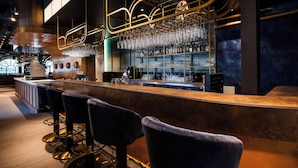 A bar area with a long counter, multiple bar stools, and a well-stocked shelf with bottles and glasses. - Efteling Wonder Hotel - Theme Park tickets included (Kaatsheuvel)