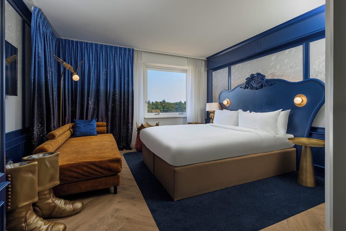 Quarto de hotel com uma cama grande, um sofá, uma mesinha de apoio e uma janela com vista.