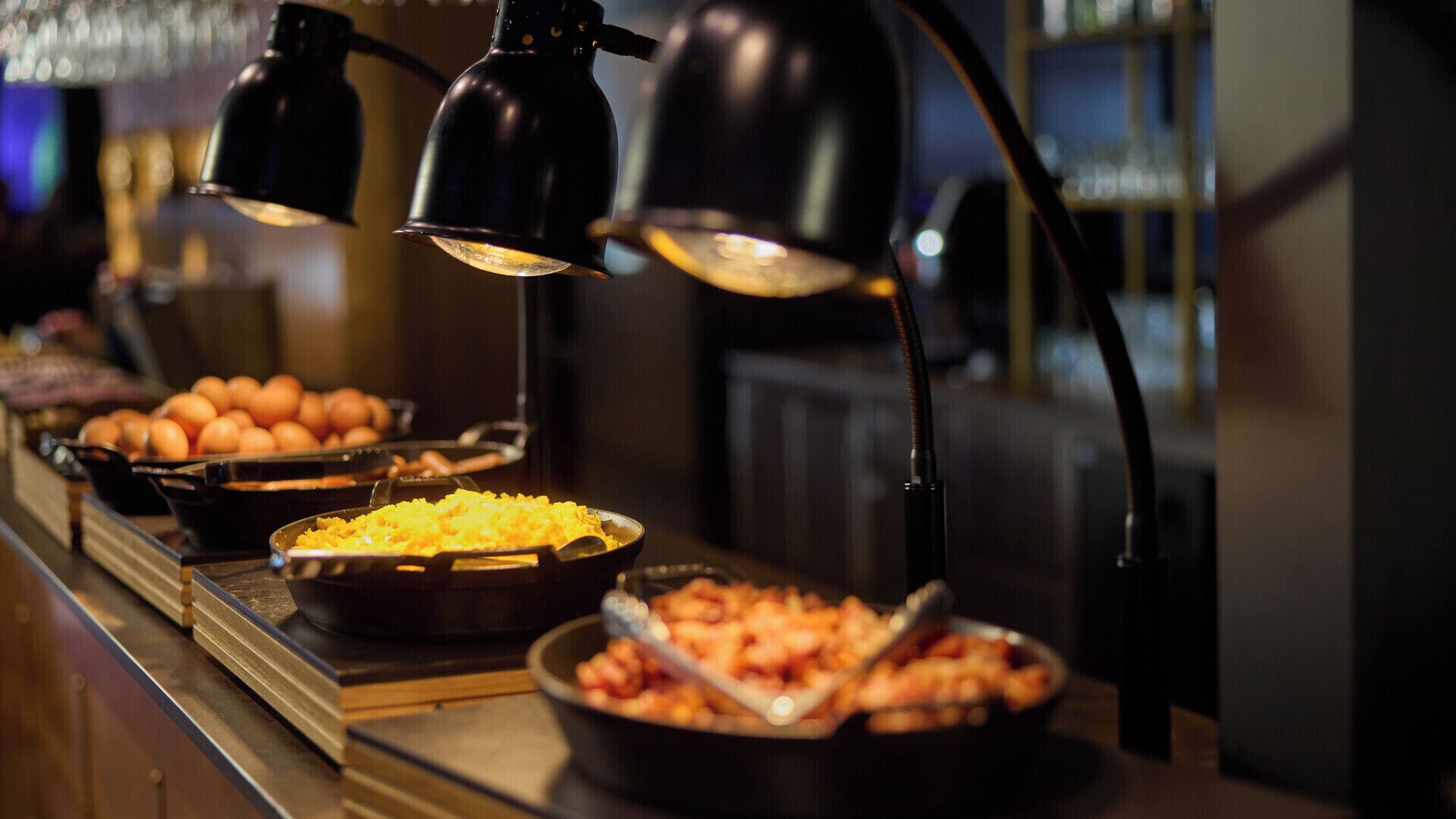 Mostrador de buffet con diversos platos, incluyendo huevos y un plato amarillo, bajo lámparas negras.