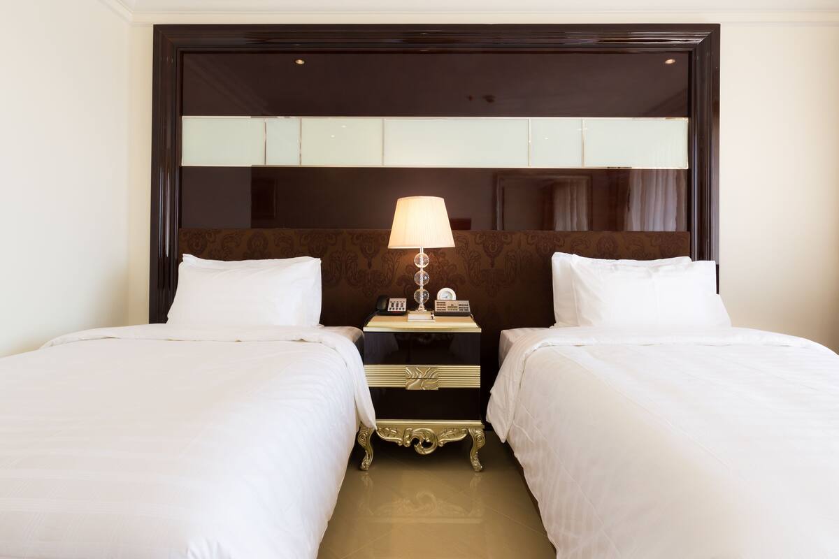 A hotel room with two beds, a nightstand with a lamp, and a large mirror above the beds.