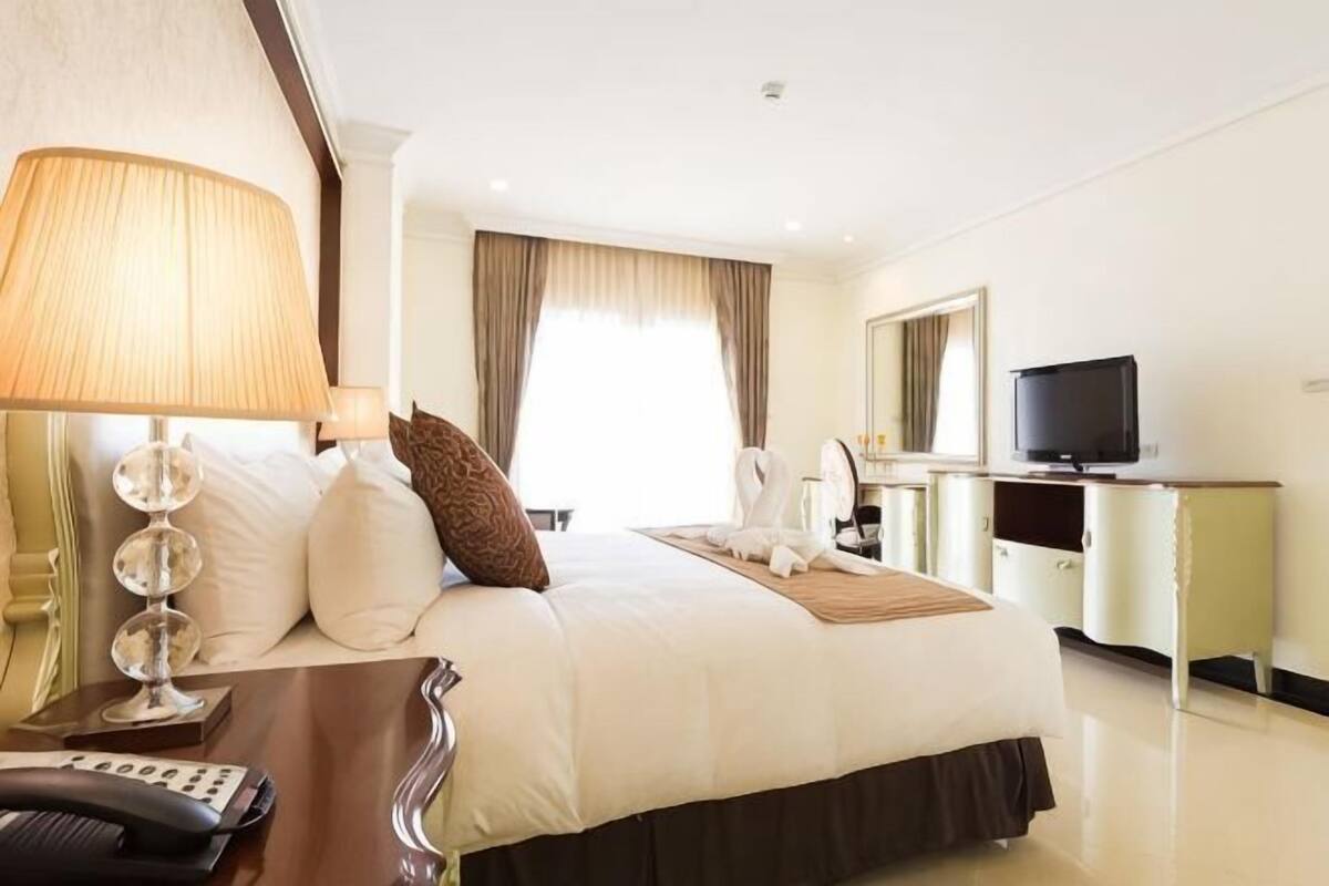 A hotel room with a bed, a bedside table with a lamp, a television, and a mirror.