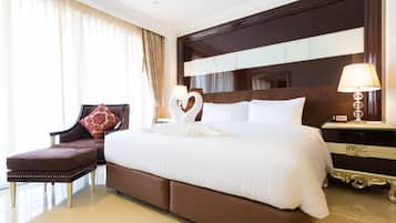 Een hotelkamer met een groot bed, een nachtkastje, een stoel en een decoratief hartvormig kussen.