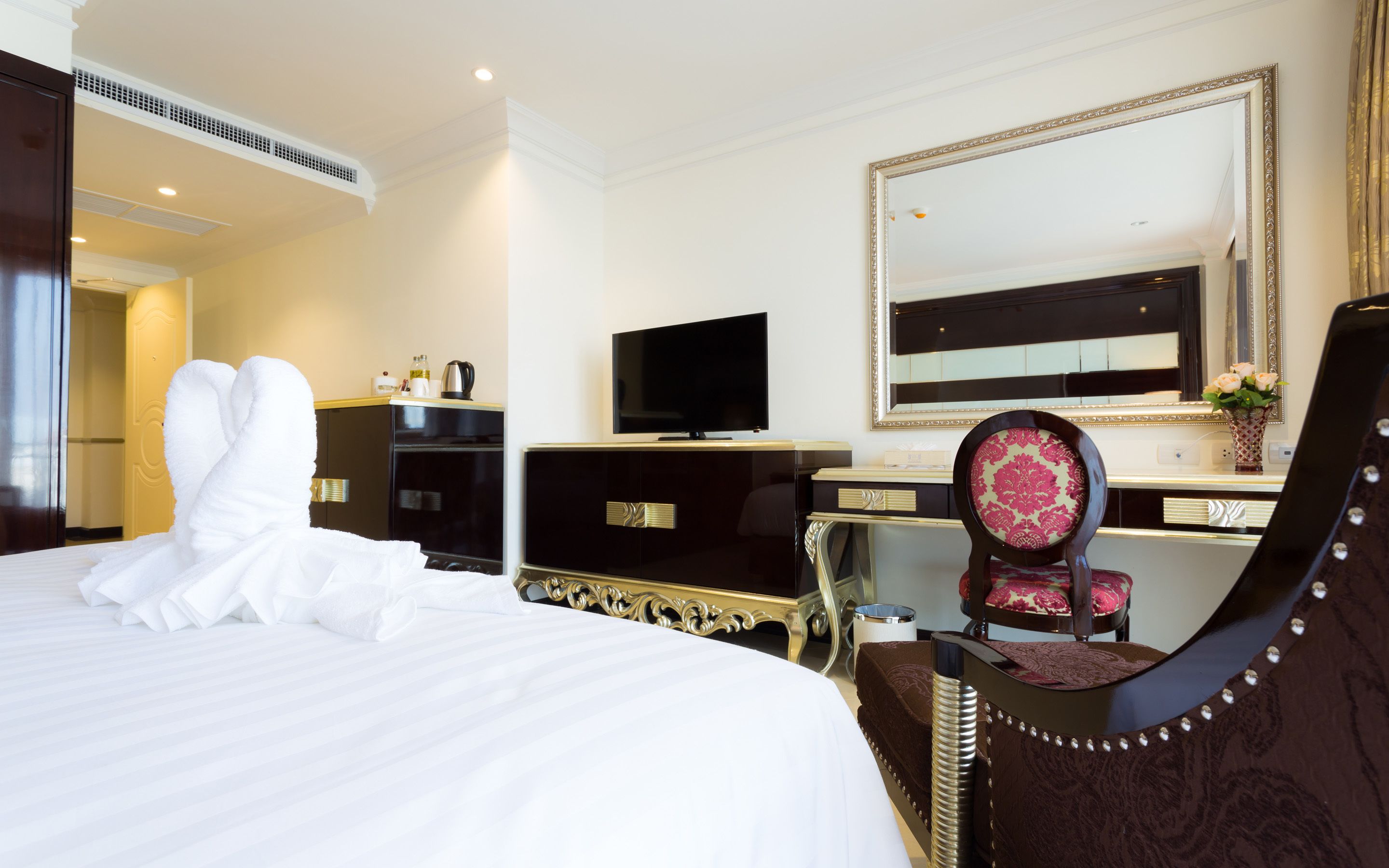 A hotel room with a large bed, a flat-screen TV, a desk with a computer, a chair, and a mirror.