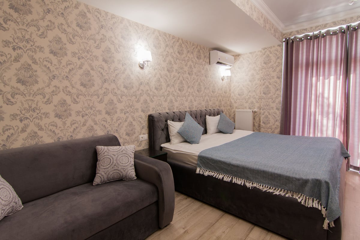 Une chambre à coucher avec un lit, un canapé, un papier peint à motifs et une fenêtre avec des rideaux.