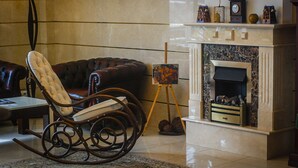 A living room with a leather sofa, a rocking chair, a fireplace, and a painting on a tripod stand. - Klassik Hotel (Chisinau)