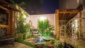 A stone pathway leading to a small waterfall and a wooden pergola with a metal spiral staircase. - Klassik Hotel (Chisinau)