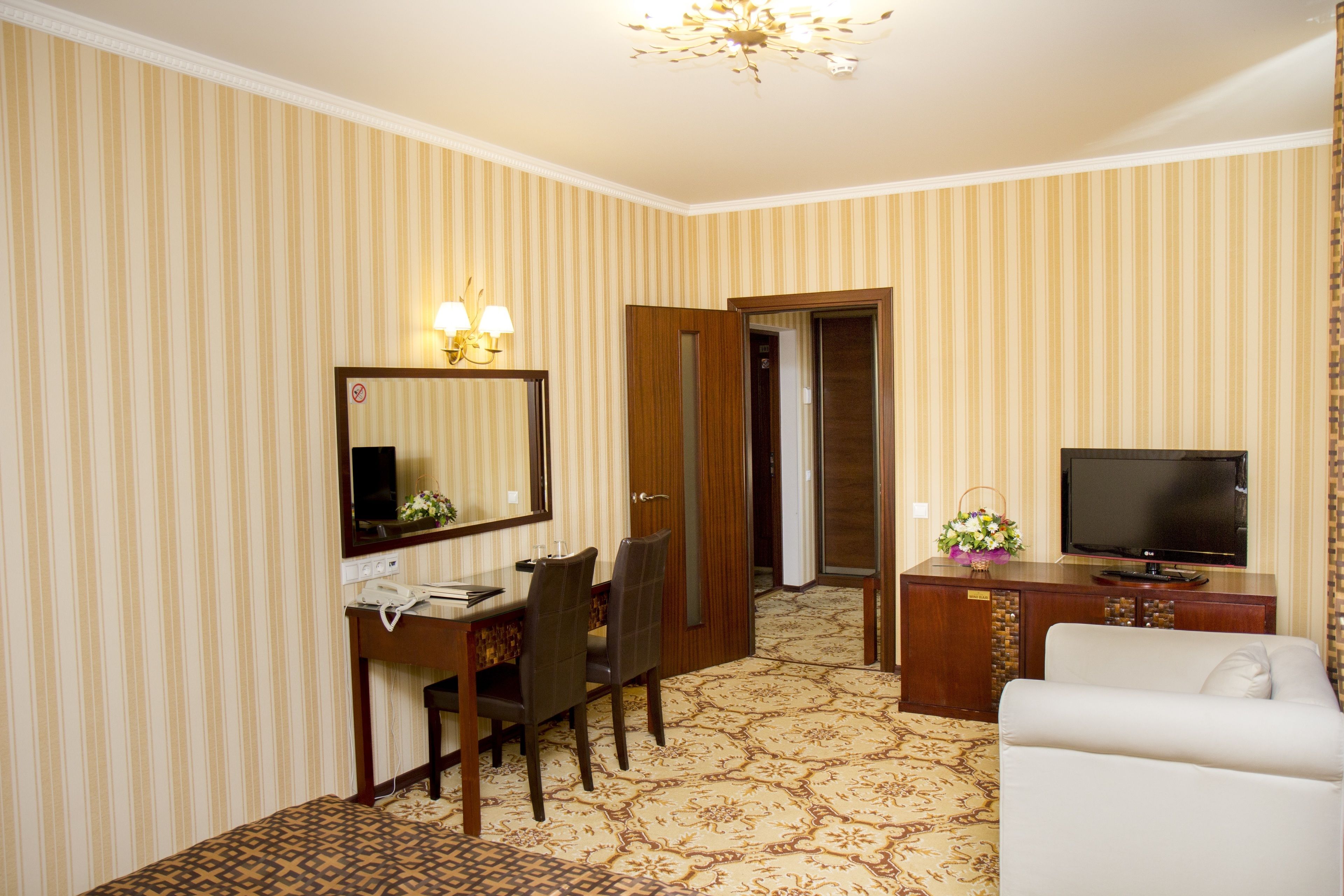 Una habitación de hotel con papel tapiz a rayas, una mesa de comedor con sillas, un televisor, un sofá y una alfombra estampada.