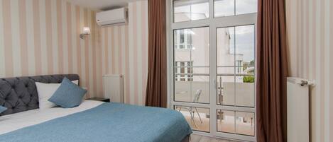 A bedroom with a bed, a window with curtains, a radiator, and a view of the outside balcony.