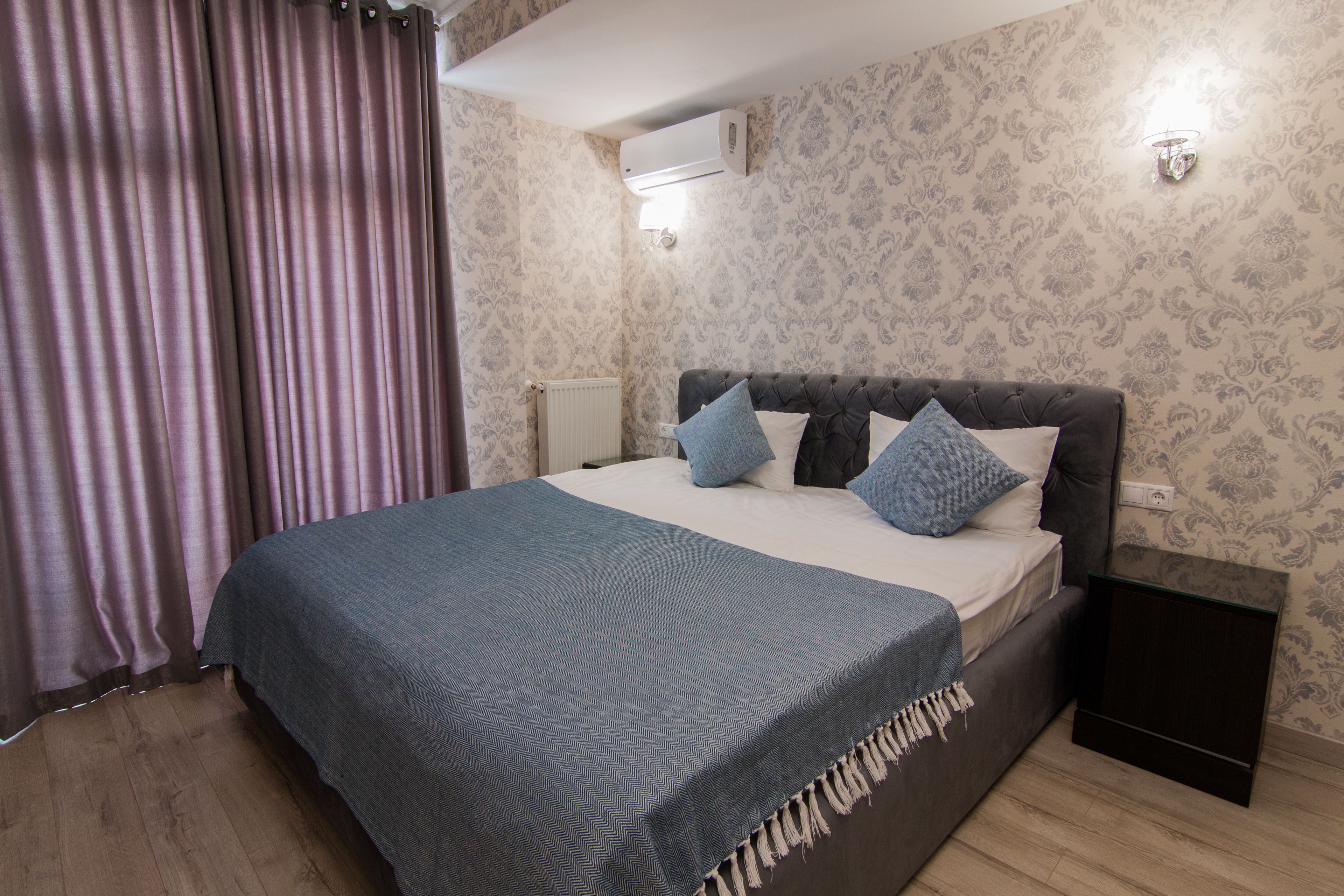 Un dormitorio con cama, mesita de noche, aire acondicionado de pared y papel tapiz estampado.
